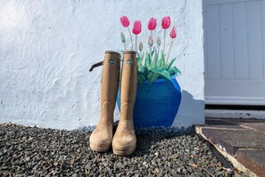 Braune Stiefel neben einem blauen Pflanzgefäß mit bemalten Blumen vor einer weißen Wand.