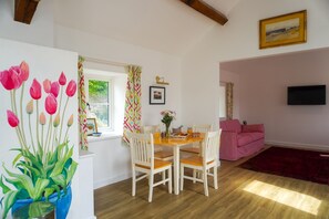 Un coin repas avec une table en bois et des chaises blanches, un canapé rose et un tapis rouge.