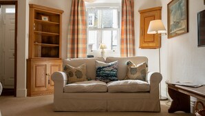 A cozy living room with a beige sofa, plaid curtains, a wooden cabinet, and a lamp. - 24 Rosemary Lane - located in the heart of Beaumari (Beaumaris)