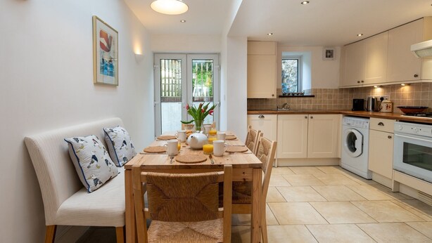 A modern kitchen with a dining area, featuring a wooden table, chairs, and a sofa with cushions. - 24 Rosemary Lane - located in the heart of Beaumari (Beaumaris)