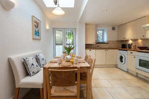 Een moderne keuken met een eethoek, met een houten tafel, stoelen en een bank met kussens.