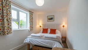 A bedroom with a bed, two bedside lamps, a window with curtains, a painting on the wall, and a wooden nightstand. - 24 Rosemary Lane - located in the heart of Beaumari (Beaumaris)