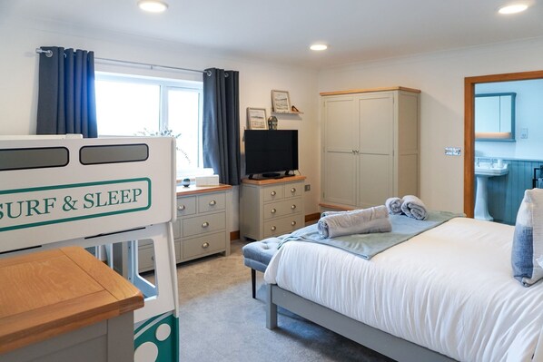 A bedroom with a bed, a TV, a wardrobe, and a small table with a sign reading 'SURF & SLEEP'.