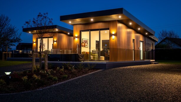 Ein modernes, zweistöckiges Haus mit großem Glasflureingang, Holzfassade und Sitzgelegenheit im Freien.