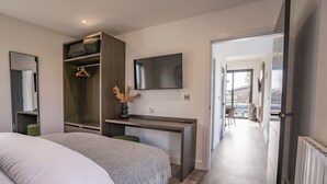 Ein modernes Hotelzimmer mit Bett, Schreibtisch mit Fernseher, Kleiderschrank und Blick ins Freie.