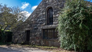 Ein Steinhaus mit einem großen Bogenfenster und einer Tür, umgeben von üppigem Grün.