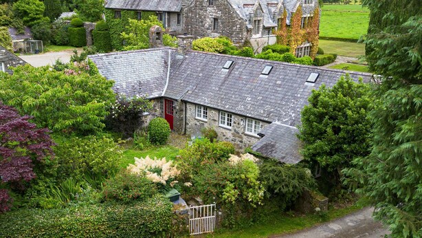 Ein Haus aus Stein mit geneigtem Dach, umgeben von üppigem Grün und einem kleinen Garten.
