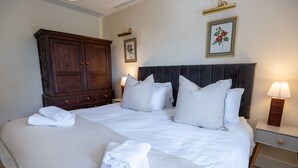 Una cama bien hecha con sábanas y almohadas blancas, un armario de madera y dos lámparas de noche.