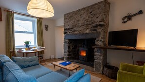 Una sala de estar acogedora con una chimenea de piedra, un sofá, un televisor y un comedor con mesa y sillas.