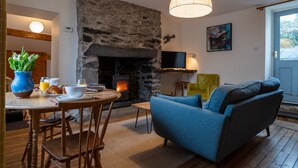 Una sala de estar acogedora con chimenea de piedra, sofá azul, muebles de madera y un comedor con productos para el desayuno.