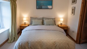 Un dormitorio con cama, dos mesitas de noche con lámparas, una ventana con cortina y un cuadro en la pared.