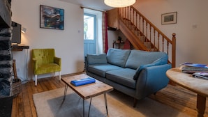 Una sala de estar acogedora con una escalera de madera, un sillón verde, un sofá gris y una mesa de centro de madera.