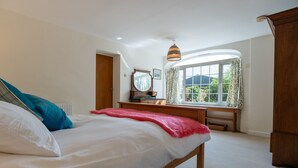 Un dormitorio con cama, un escritorio de madera, un espejo y una ventana con cortinas.