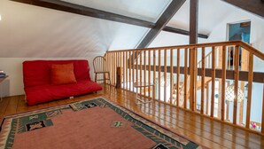 Un dormitorio estilo loft acogedor, con un sofá rojo, un tapete estampado y una barandilla de madera con vistas a un balcón.