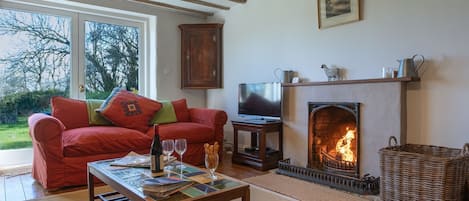 Una sala de estar acogedora con chimenea, un sofá, un televisor y una mesa con una botella y vasos.