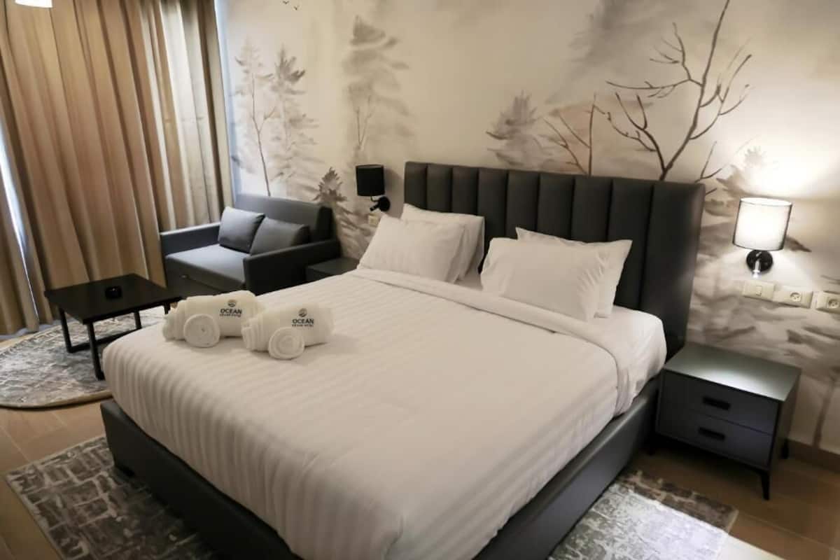 Une chambre d’hôtel avec un grand lit, un canapé, une table de chevet et un mur décoré d’un motif représentant un arbre.