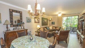 A dining area with a round table, chairs, and a chandelier. There is a sofa and a television in the living area. - Recently Renovated • Pacifico L604 Casa Xanadu • 2 BR Ground Floor Condo • Playas del Coco (Playas del Coco)