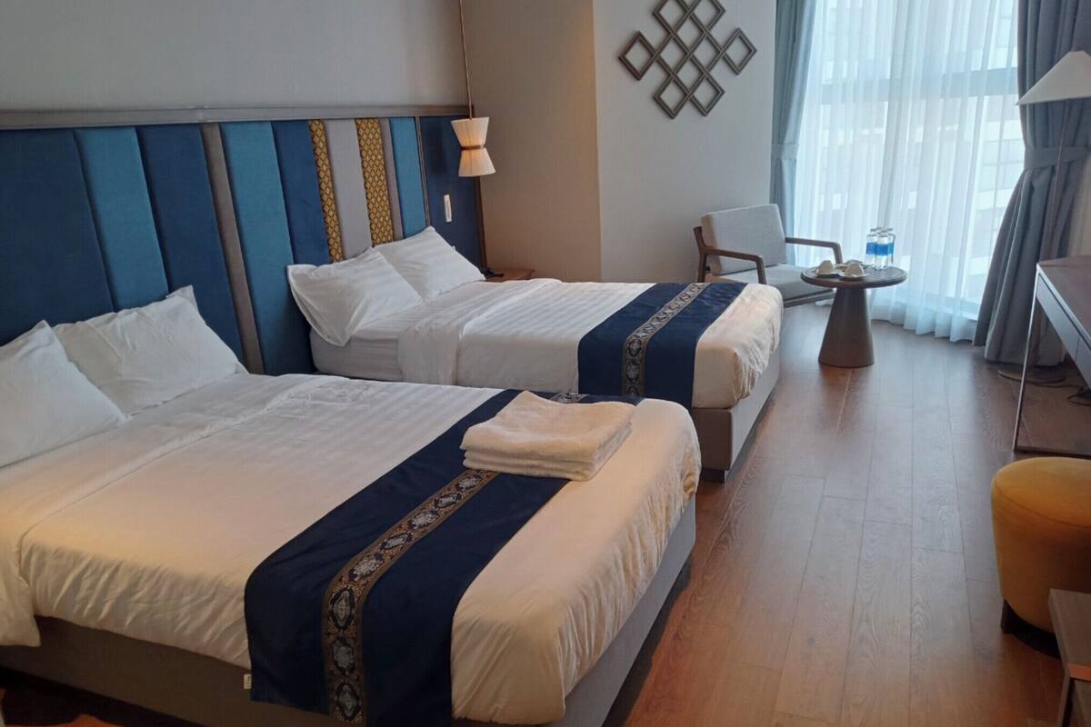 A hotel room with two beds, a desk, a chair, and a small table.