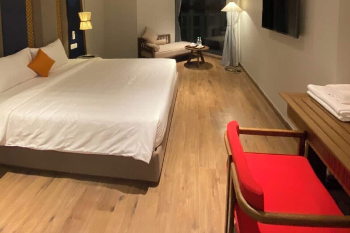 A hotel room with a large bed, bedside tables, a TV, and a red chair.