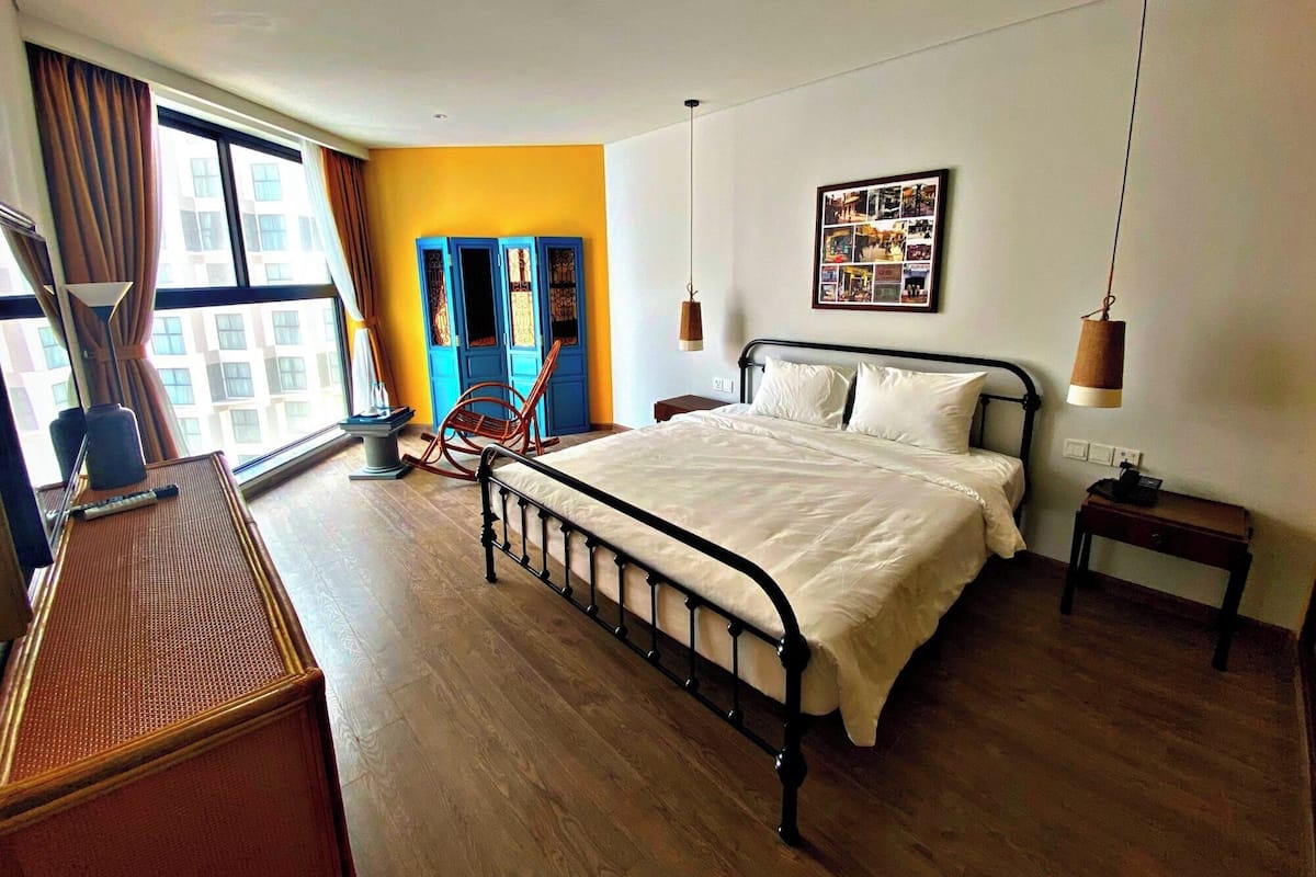 A hotel room with a bed, a desk with a lamp, a chair, a wardrobe, and a picture on the wall.