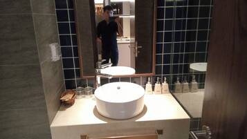 A bathroom with a round sink, a mirror, and a towel rack.