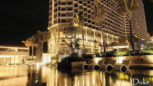 Un hôtel de grande hauteur doté d’une façade géométrique remarquable, d’un espace piscine avec des chaises longues et de palmiers.