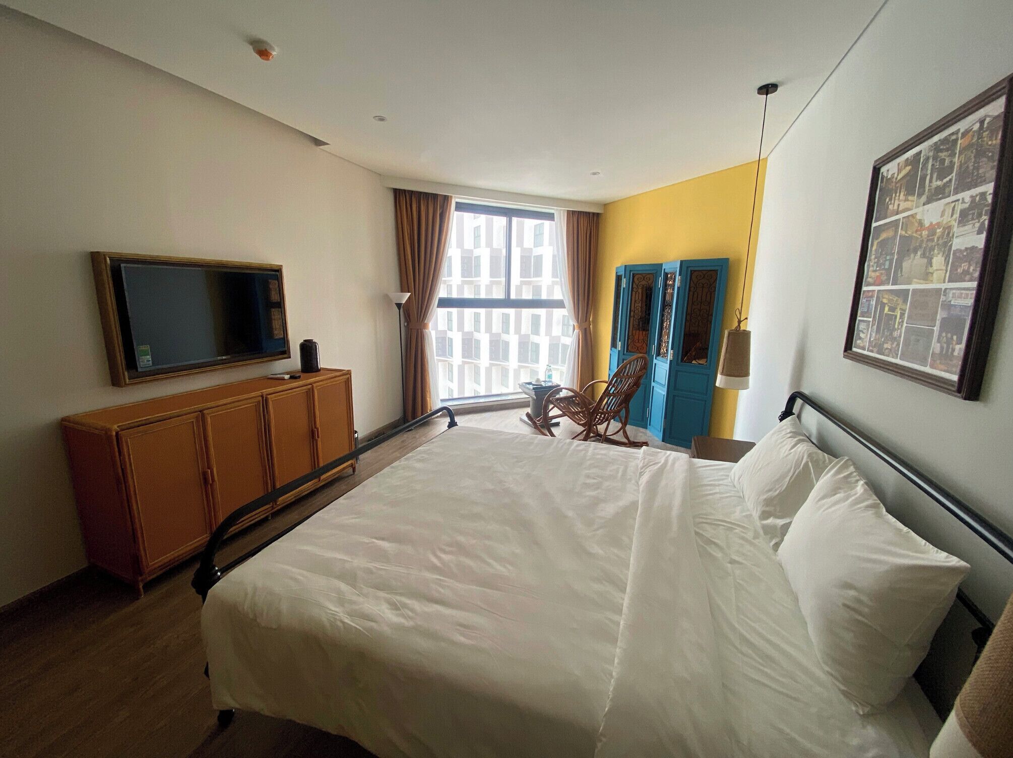 A hotel room with a large bed, a television on a wooden cabinet, a rocking chair, and a window with curtains.