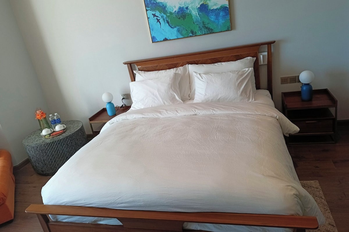 A neatly made bed with white linens, a wooden headboard, and two bedside tables with lamps.