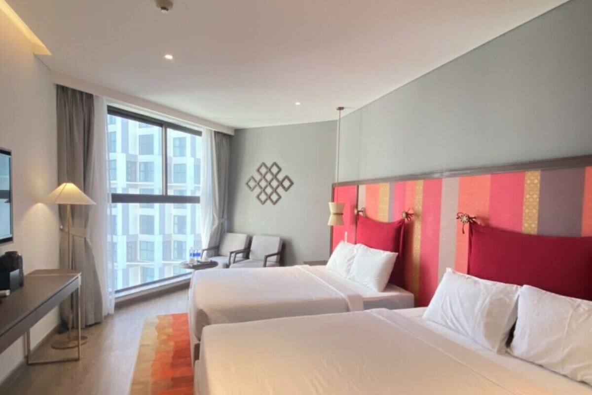 A hotel room with two beds, a desk, a chair, and a large window.