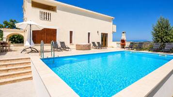 A modern hotel with a swimming pool, outdoor seating, and a view of the sea.
