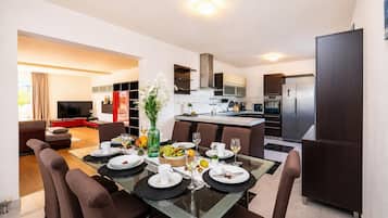 A modern kitchen with a dining area, a TV in the living room, and a large window.