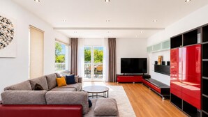 Una sala moderna con un sofá gris, un detalle rojo, un televisor de pantalla plana y un aparador de vidrio.