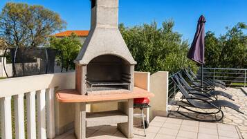 An outdoor stone-built pizza oven with a bench, surrounded by a tiled patio and lounge chairs.