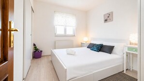 Una habitación de hotel con cama, mesita de noche, lámpara, ventana, radiador y puerta.