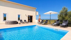 Una piscina con sillas de descanso y una sombrilla, un jacuzzi y un edificio con puerta y ventanas.