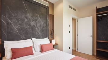 Una habitación de hotel moderna con una cama grande, cabecera de mármol, armario de madera y una puerta blanca.