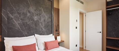 A modern hotel room with a large bed, a marble headboard, a wooden wardrobe, and a white door.