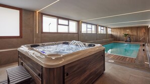 A modern indoor swimming pool area with a hot tub, wooden panel walls, and large windows.
