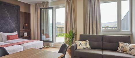 Habitación de hotel con cama, sofá, mesa de comedor y balcón con vistas.