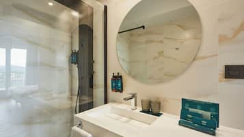 A modern bathroom with a large mirror, a glass shower enclosure, and a vanity with a sink and two bottles of shampoo.