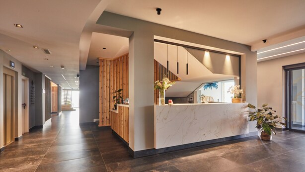A spacious hallway with a reception desk, wooden paneling, and a potted plant.