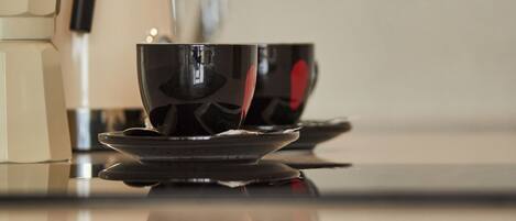 Una encimera de cocina con una cafetera, un hervidor y una taza en su platillo.