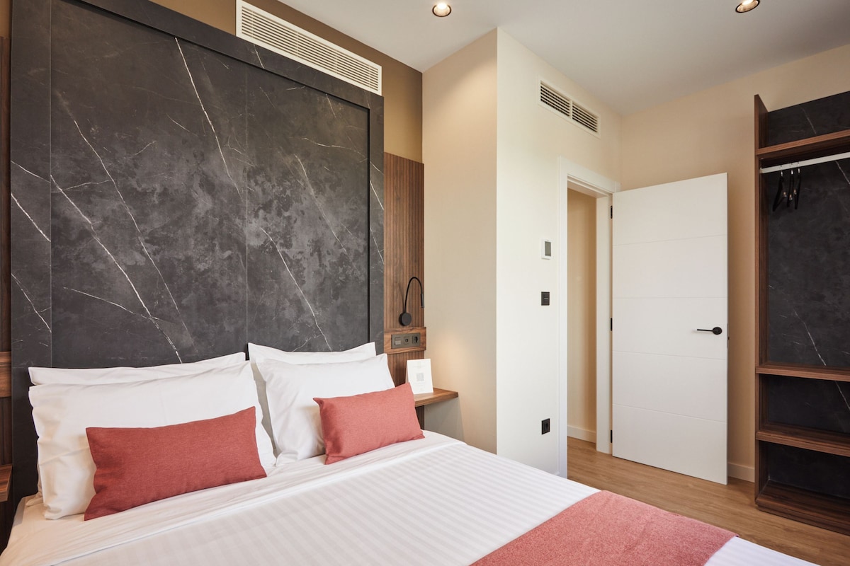 A modern hotel room with a large bed, a marble headboard, a wooden wardrobe, and a white door.
