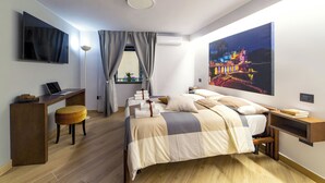 Een moderne hotelkamer met een bed, bureau en stoel, een groot raam met gordijnen, en een schilderij aan de muur.