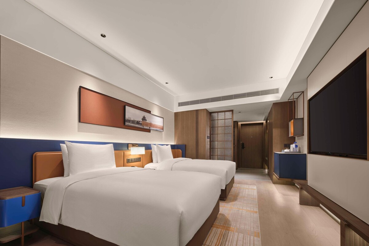 A hotel room with two beds, a TV, a desk, and a bathroom door.