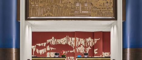 A hotel reception area with a modern design, featuring a reception desk, two chairs, and a decorative wall with abstract patterns.