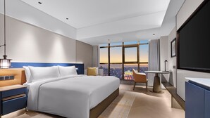 Een moderne hotelkamer met een groot bed, een bureau, een stoel en een groot raam met uitzicht op de stad.