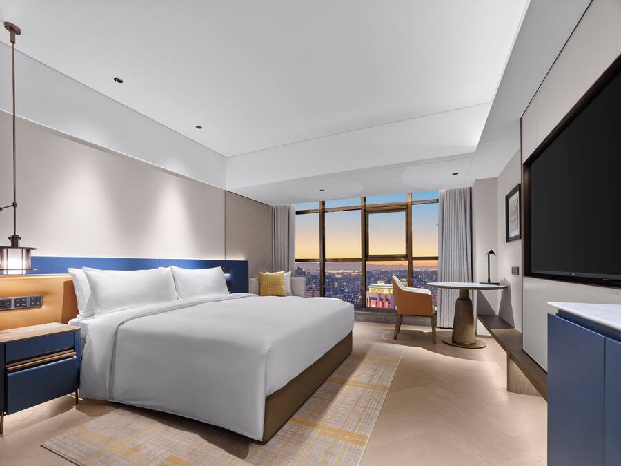 Een moderne hotelkamer met een groot bed, een bureau, een stoel en een groot raam met uitzicht op de stad.