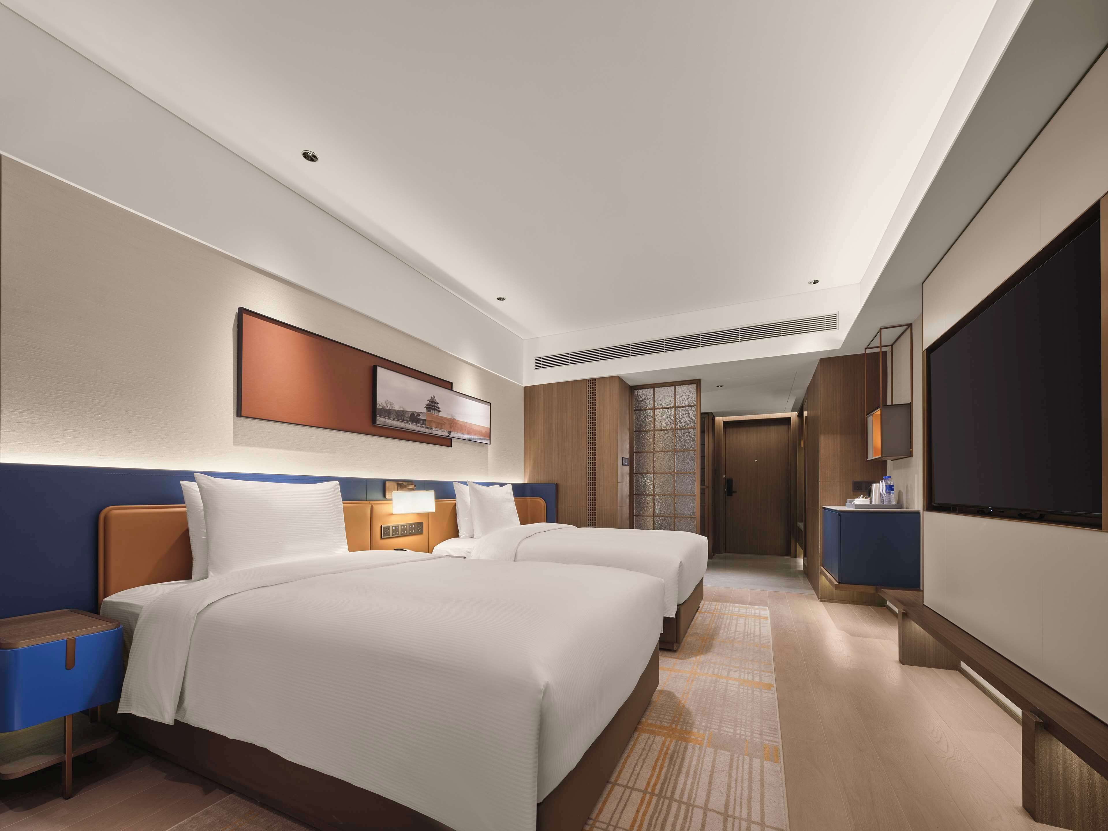 A hotel room with two beds, a TV, a desk, and a bathroom.