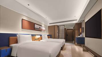 A hotel room with two beds, a TV, a desk, and a bathroom.
